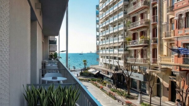 A balcony with a view of the sea, a street with buildings, and a sign for 'Hotel de la Mer.' - Pillow by the Sea (Thessaloniki)