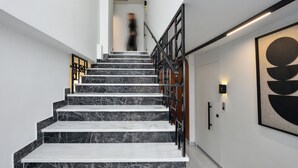 A staircase with marble steps and a metal railing, leading to a door with a light switch and a framed artwork on the wall. - Pillow by the Sea (Thessaloniki)