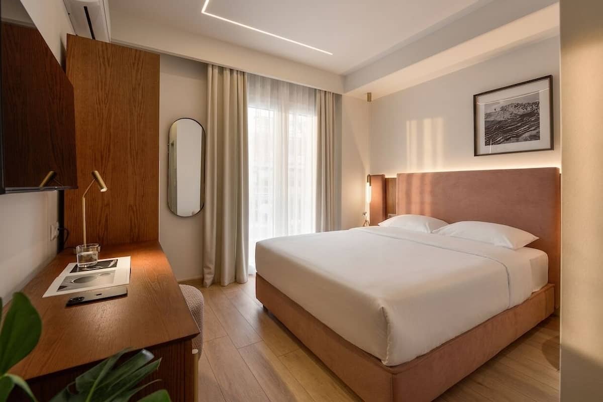 Una habitación de hotel con una cama, un escritorio, un espejo y una ventana con cortinas.