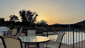 An outdoor patio with a round table and chairs, a swimming pool, and a view of trees and hills during sunset. - Cortijo Huerta Galindo (Alanís)
