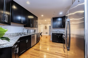 A modern kitchen with dark cabinets, stainless steel appliances, and a wooden floor.