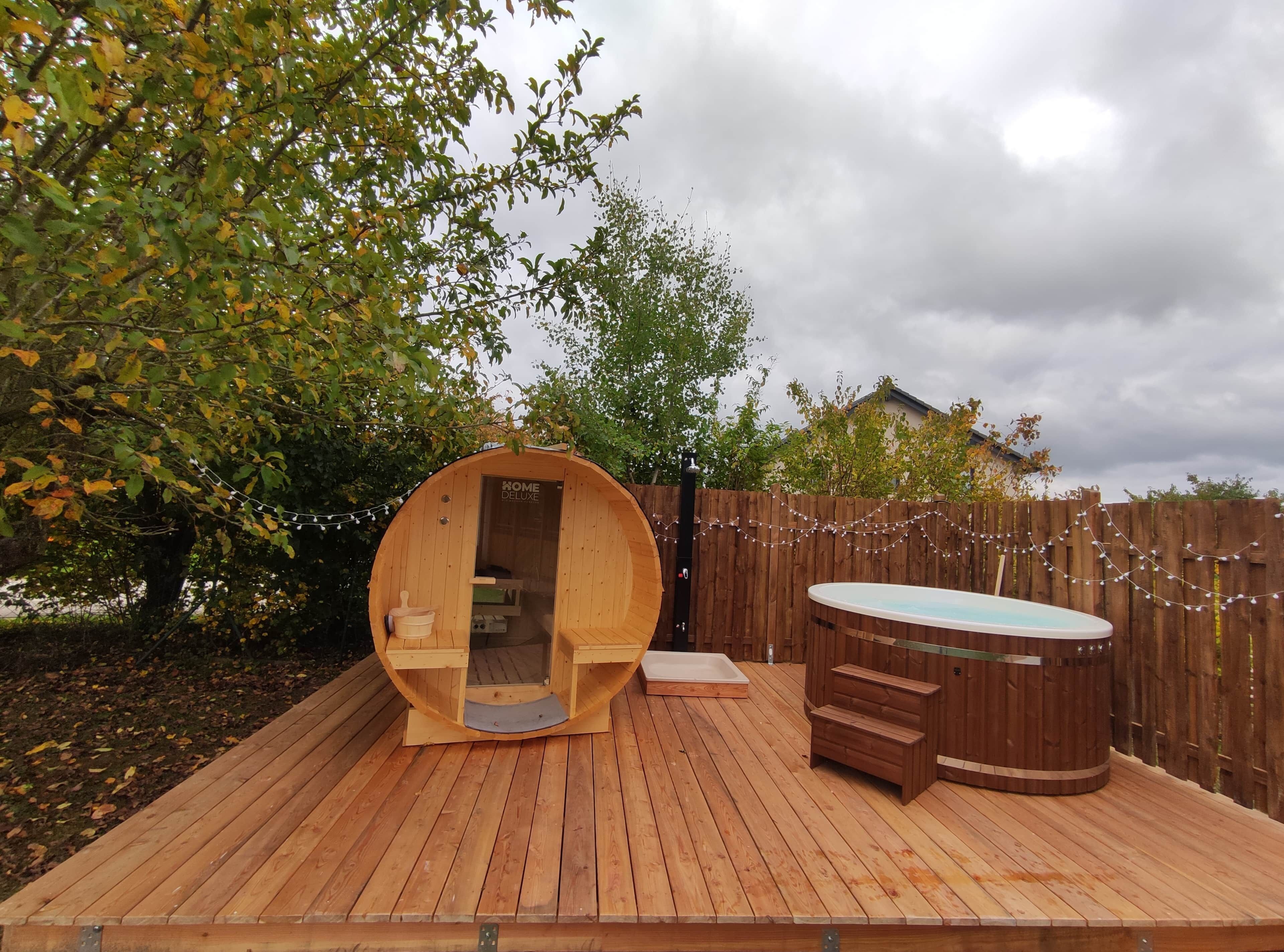 Een houten terras met een sauna, een jacuzzi en een houten hek.