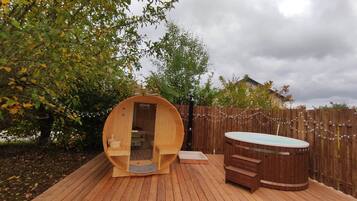 Een houten terras met een sauna, een jacuzzi en een houten hek.