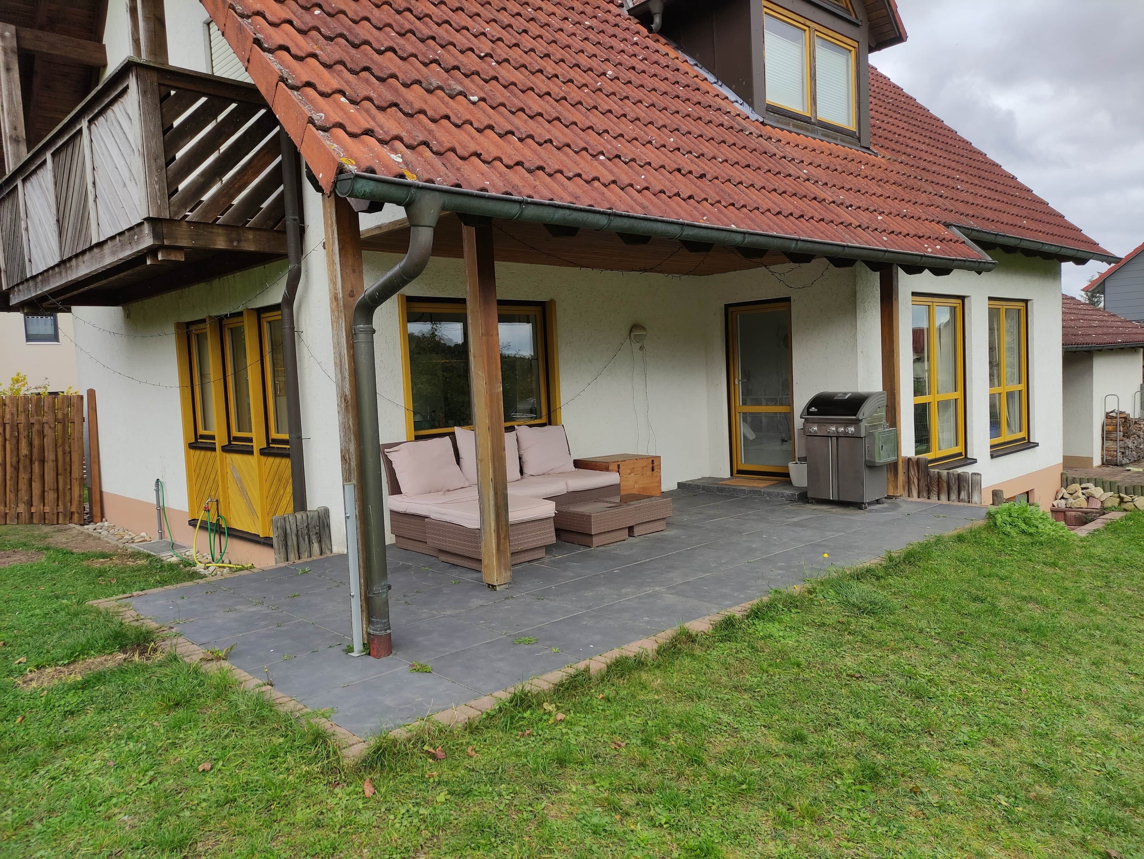 Une maison avec un porche, un barbecue et une cour clôturée.