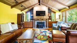 Een ruime woonkamer met een open haard, leren banken en een kleurrijk vloerkleed.