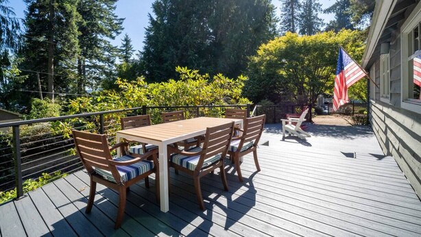 Een houten terras met een tafel en stoelen, omgeven door groen en bomen.