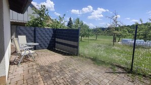 A patio area with a brick floor, a table with chairs, and a blue fence. - Fox den in the holiday home at the Holzecke (Schnelldorf)