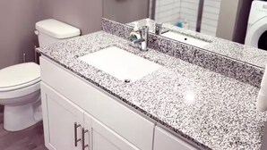 A modern bathroom with a white toilet, granite countertop sink, and a large mirror.
