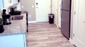 A kitchen with white cabinets, a stainless steel refrigerator, and a trash can.