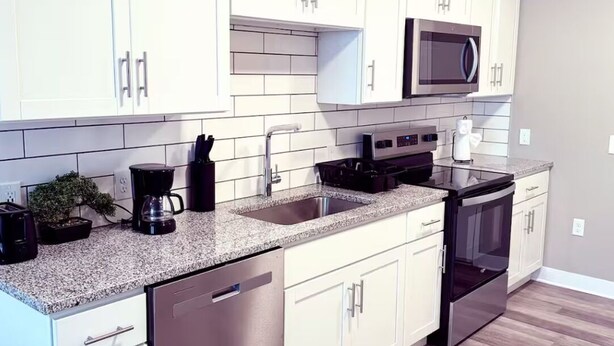A modern kitchen with white cabinets, a stainless steel dishwasher, a microwave, and a stove.