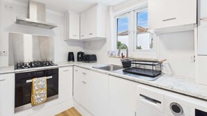 A modern kitchen with white cabinetry, a gas stove, a coffee maker, and a window with a view.