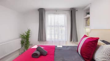 A modern hotel room with a bed, a window with curtains, a radiator, and a small plant.