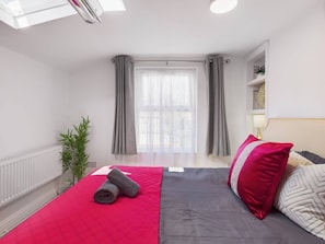 Ein modernes Hotelzimmer mit einem Bett, einem Fenster mit Vorhängen, einem Heizkörper und einer kleinen Pflanze.