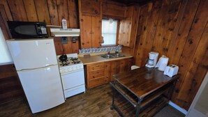 A compact kitchen with wooden walls, a white refrigerator, a stove, a microwave, a sink, and a coffee maker. - Cabin 2 @ Lazy Day Cabins (Mayhill)