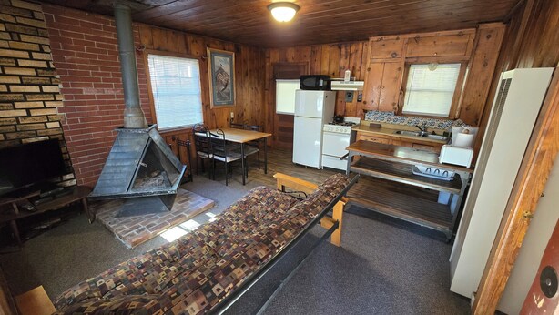 A compact kitchen with a stove, microwave, refrigerator, and a dining area with a table and chairs. - Cabin 2 @ Lazy Day Cabins (Mayhill)
