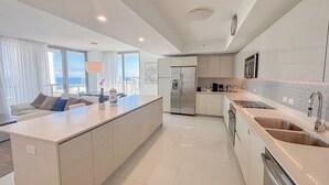 A modern kitchen with a central island, stainless steel appliances, and a view of the city. - Luxury 3-BR Apartment with Stunning City (Hallandale Beach)