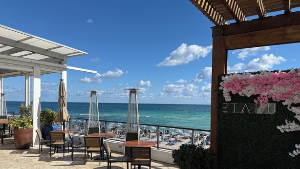 A terrace with tables and chairs, a view of the beach, and a sign with 'ETARU' on a wall. - Luxury 3-BR Apartment with Stunning City (Hallandale Beach)