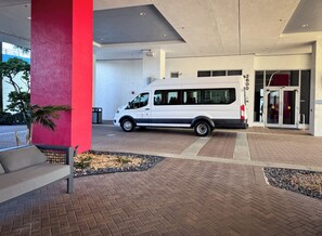 A white van parked outside a building with a red pillar, a bench, and a paved entrance area. - Luxury 3-BR Apartment with Stunning City (Hallandale Beach)