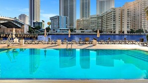 A poolside area with lounge chairs and umbrellas, a waterfront view, and high-rise buildings in the background. - Luxury 3-BR Apartment with Stunning City (Hallandale Beach)