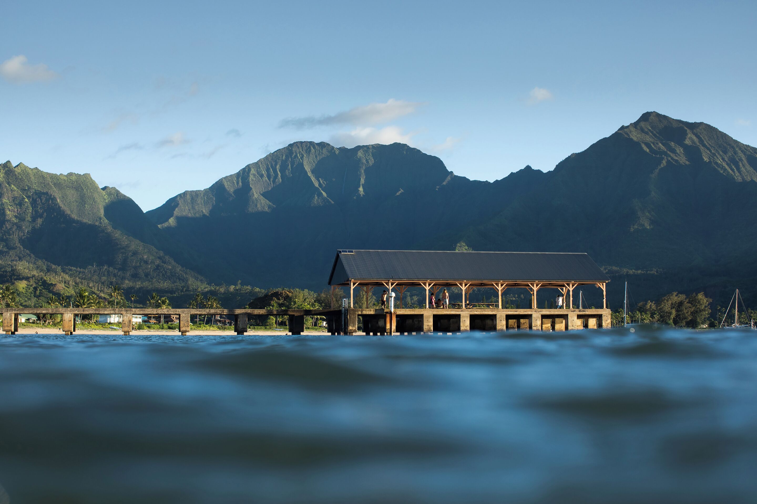 A building with a wooden structure and a flat roof, situated by a body of water with mountains in the background.