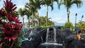 A tropical resort with a waterfall, palm trees, and a pool.
