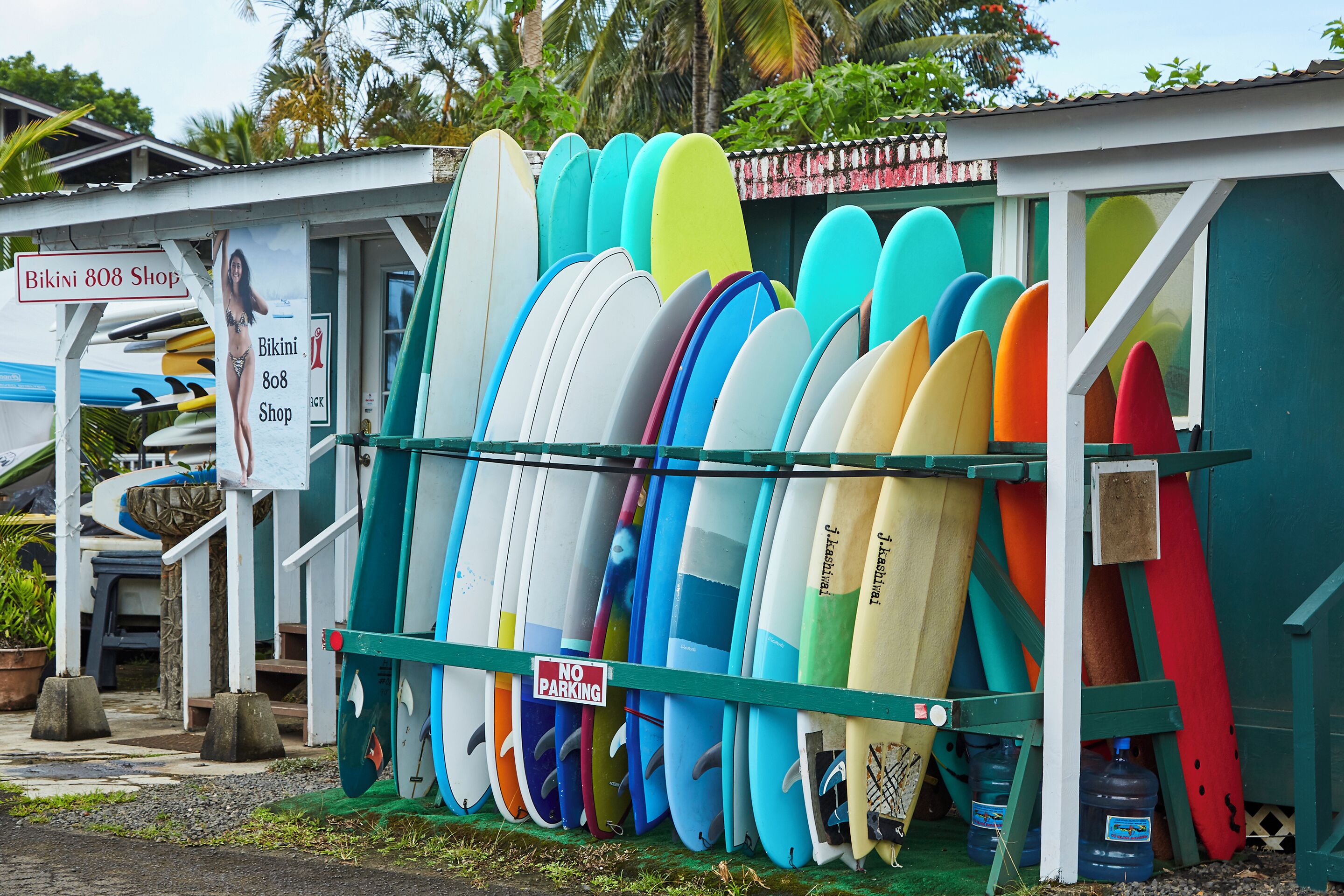 A row of colorful surfboards leaning against a wall with a 'No Parking' sign.