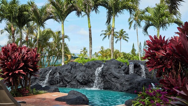 A tropical resort with a pool, palm trees, and a waterfall.