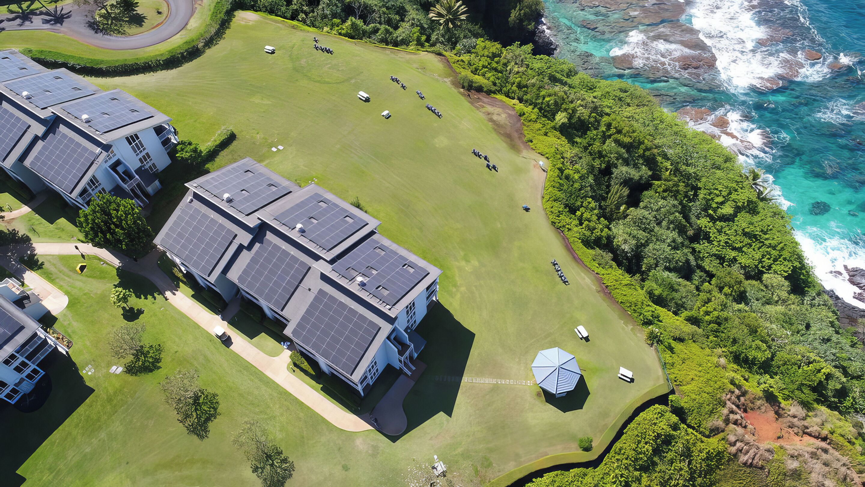 A residential area with solar panel-equipped buildings, a well-maintained lawn, and a view of the ocean.