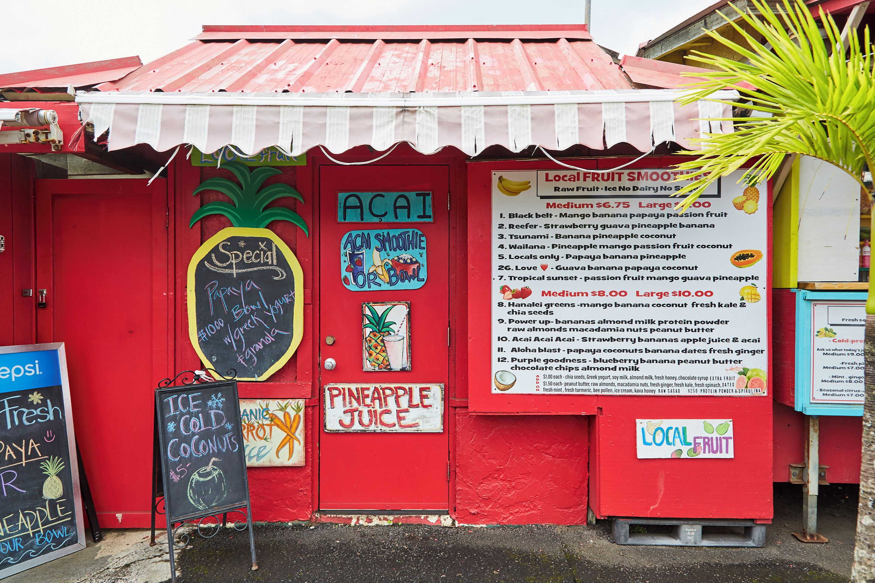A red storefront with a sign for 'ACAI Smoothie for Bowl' and a menu for local fruit smoothies.