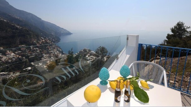 A balcony with a view of a coastal town, a table with lemons and bottles, and decorative blue and green ornaments. - Villa Dei Srls (Positano)