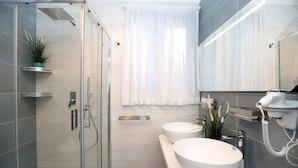 A modern bathroom with a glass shower enclosure, two white sinks, a large mirror, and a hairdryer on a wall-mounted shelf. - Villa Dei Srls (Positano)