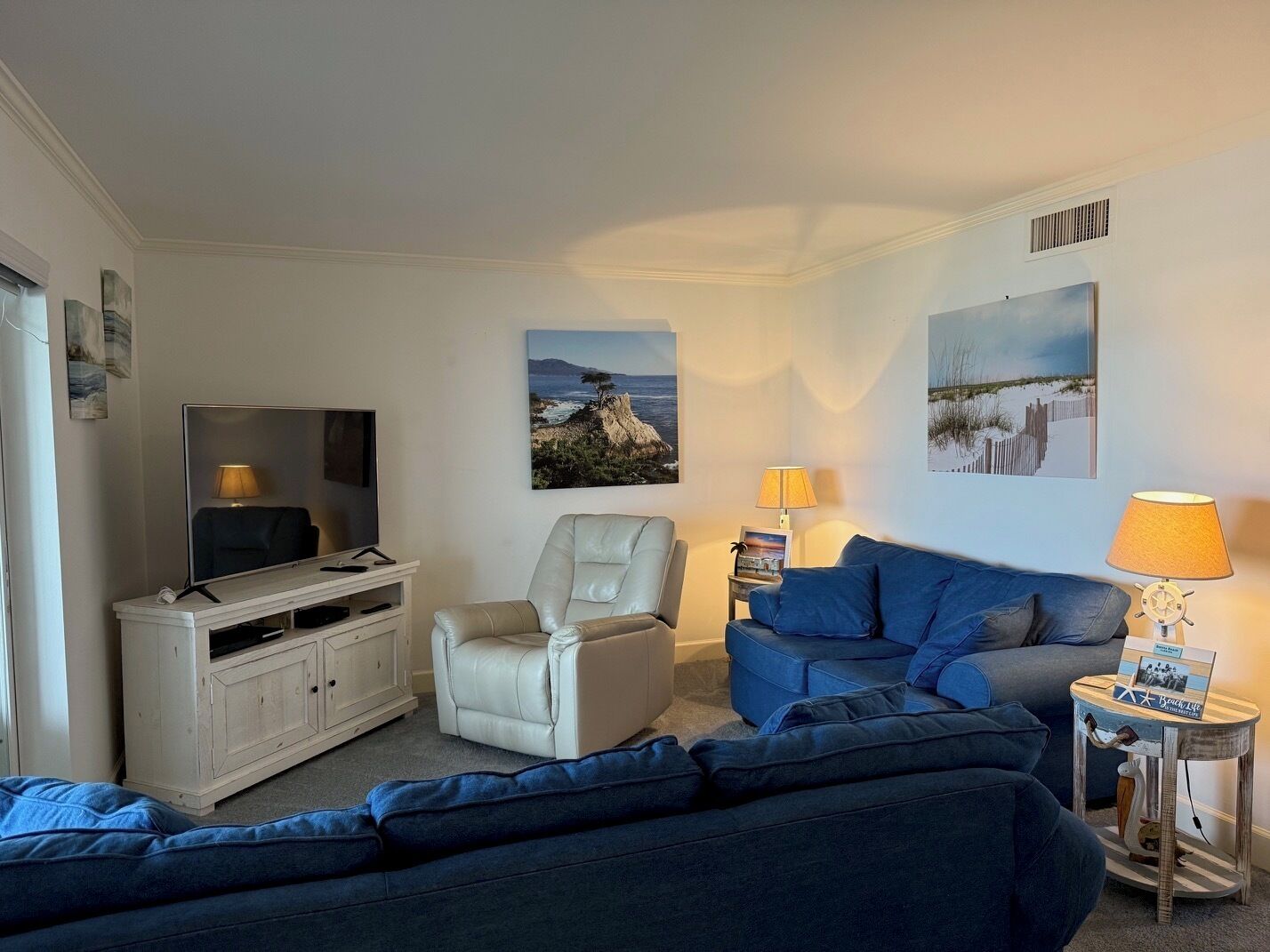 A living room with a TV, a sofa, a chair, and a small table with a lamp.