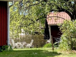 A red barn with a covered entrance, a wooden fence, and a grassy area with a white chair. - 5 Person Holiday Home in Tving (Tving)
