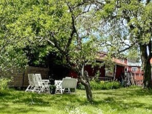 Un giardino con tavolo e sedie, un albero e un edificio rosso sullo sfondo.