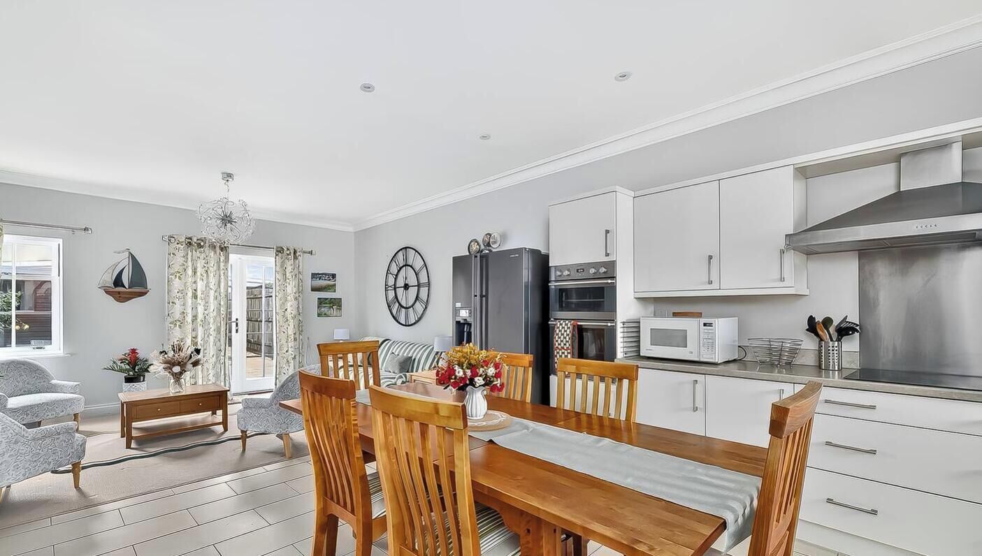 A modern kitchen with white cabinets, stainless steel appliances, and a dining area with wooden furniture.