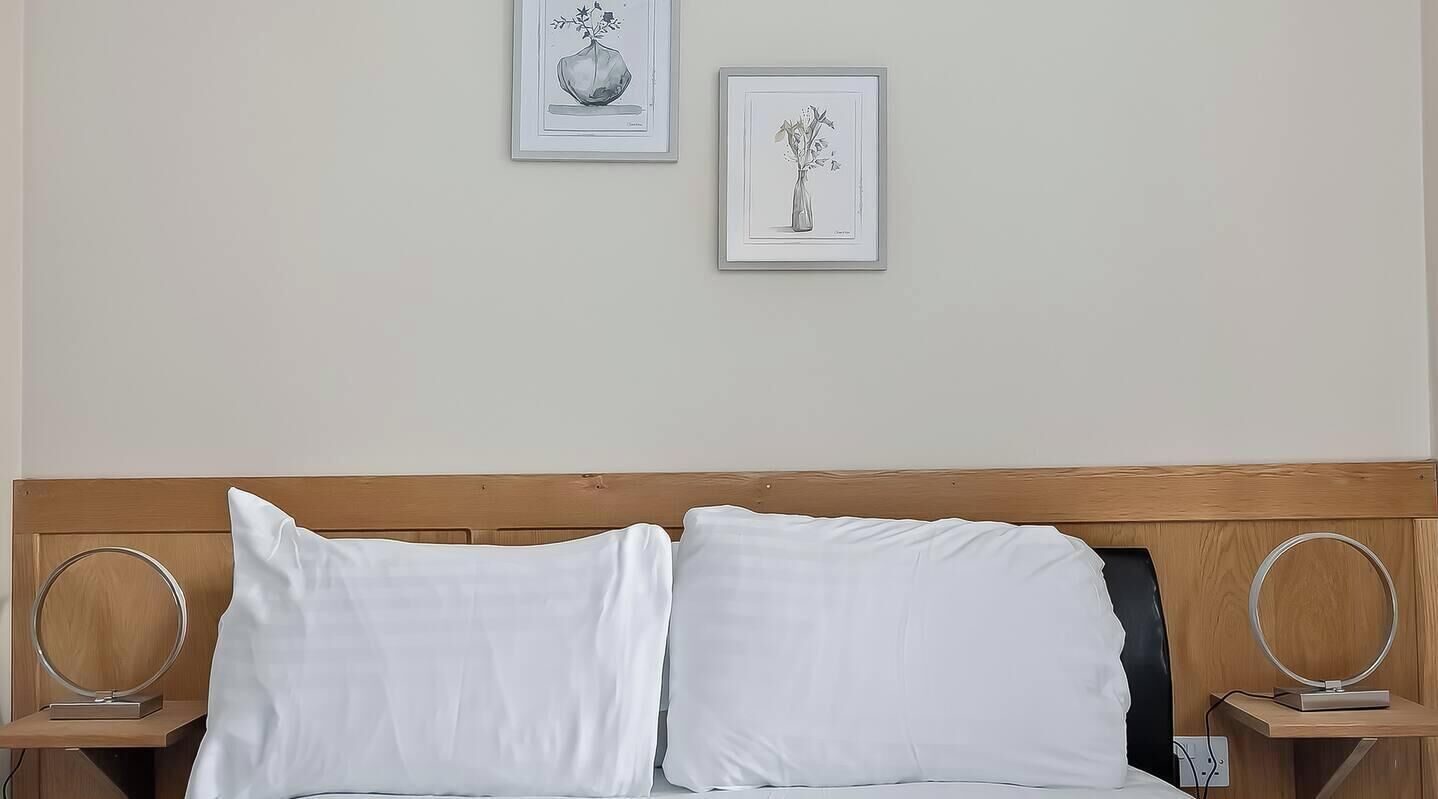 Cama com roupa de cama branca, cabeceira de madeira e duas mesas de cabeceira com espelhos redondos.