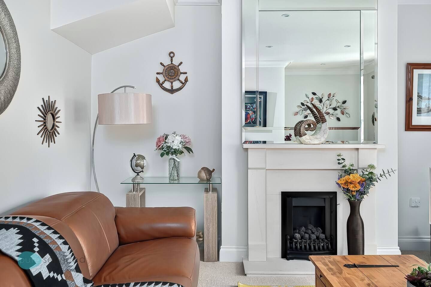 A modern living room with a leather sofa, a glass coffee table, a fireplace, and decorative wall art.