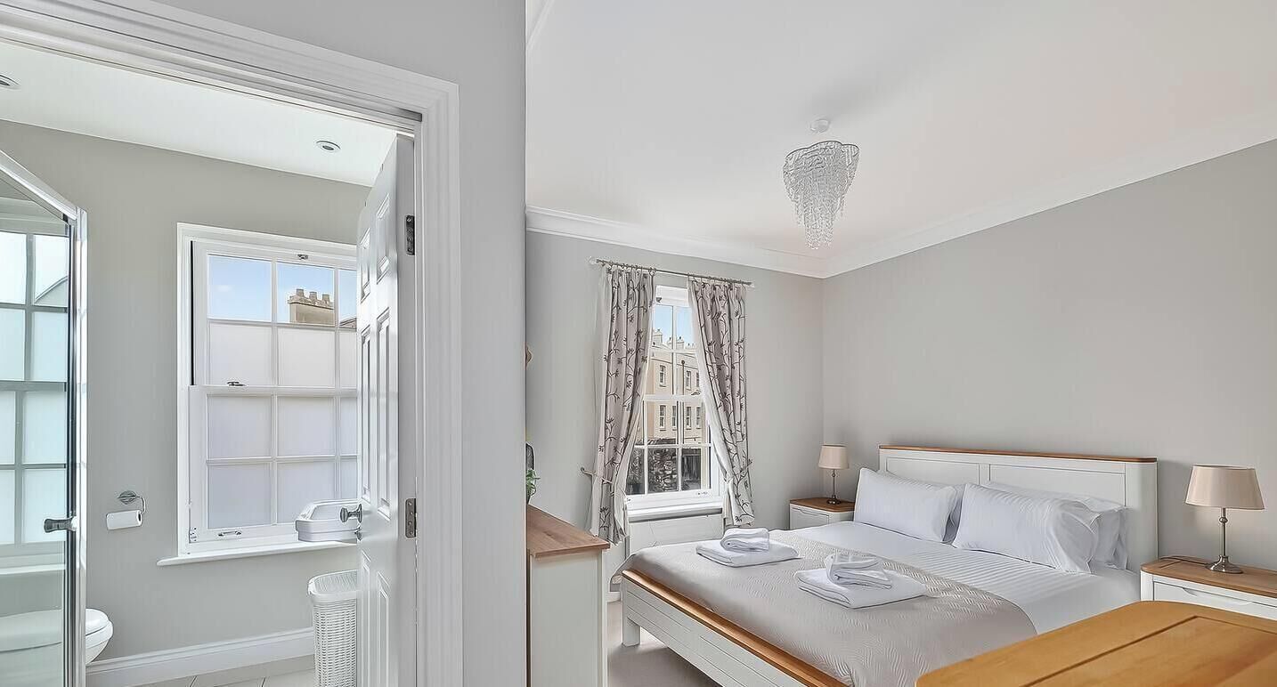 Una habitación de hotel con cama, mesitas de noche, ventana con cortinas y un candelabro.
