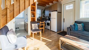 Eine moderne Küche mit Holzbalken, ein Essbereich mit Stuhl und Tisch sowie ein Wohnzimmer mit Sofa und Kissen.