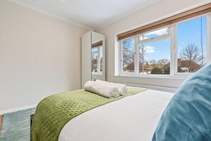 A bedroom with a bed, a window, a mirror, and a view of houses outside. - Charming Thames Ditton Apt- Sleeps 6- Free Parking (Thames Ditton)