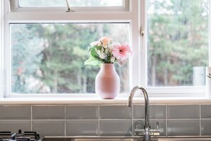 Uma cozinha com janela, um vaso rosa com flores e uma torneira.
