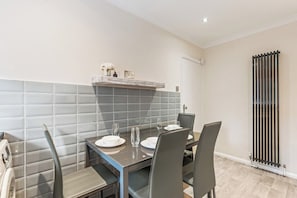 Een eethoek met een tafel voor vier personen, een grijze betegelde spatwand en een radiator aan de muur.