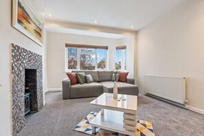 A modern living room with a fireplace, a sectional sofa, a coffee table, and large windows. - Charming Thames Ditton Apt- Sleeps 6- Free Parking (Thames Ditton)