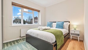 A bedroom with a bed, a nightstand, a window, and a radiator. - Charming Thames Ditton Apt- Sleeps 6- Free Parking (Thames Ditton)