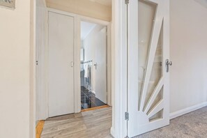 Um corredor com piso de madeira, porta branca e porta de vidro que dá para uma escada.