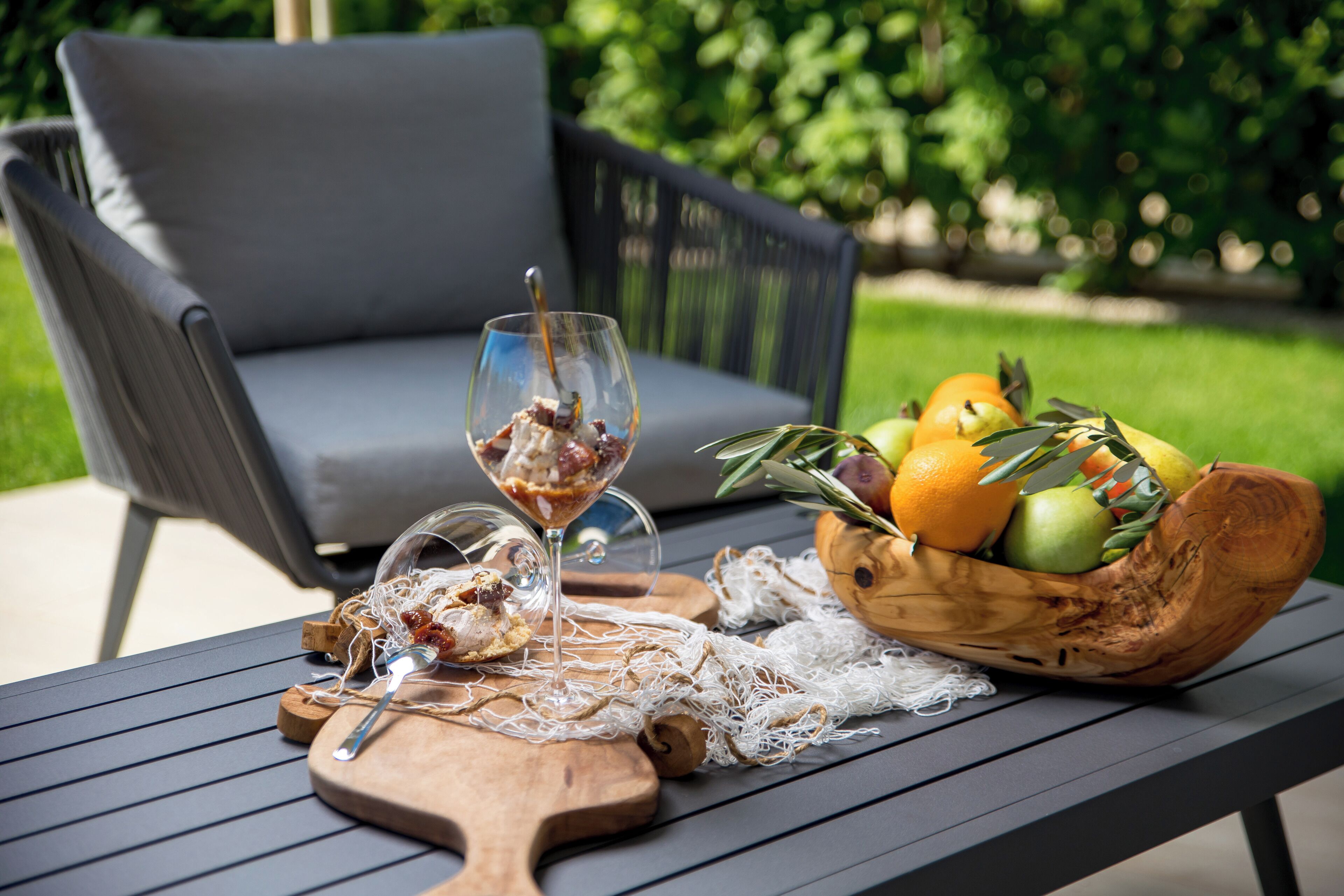 A table with a fruit bowl, a glass of drink, and a wooden board with a knife and fork.