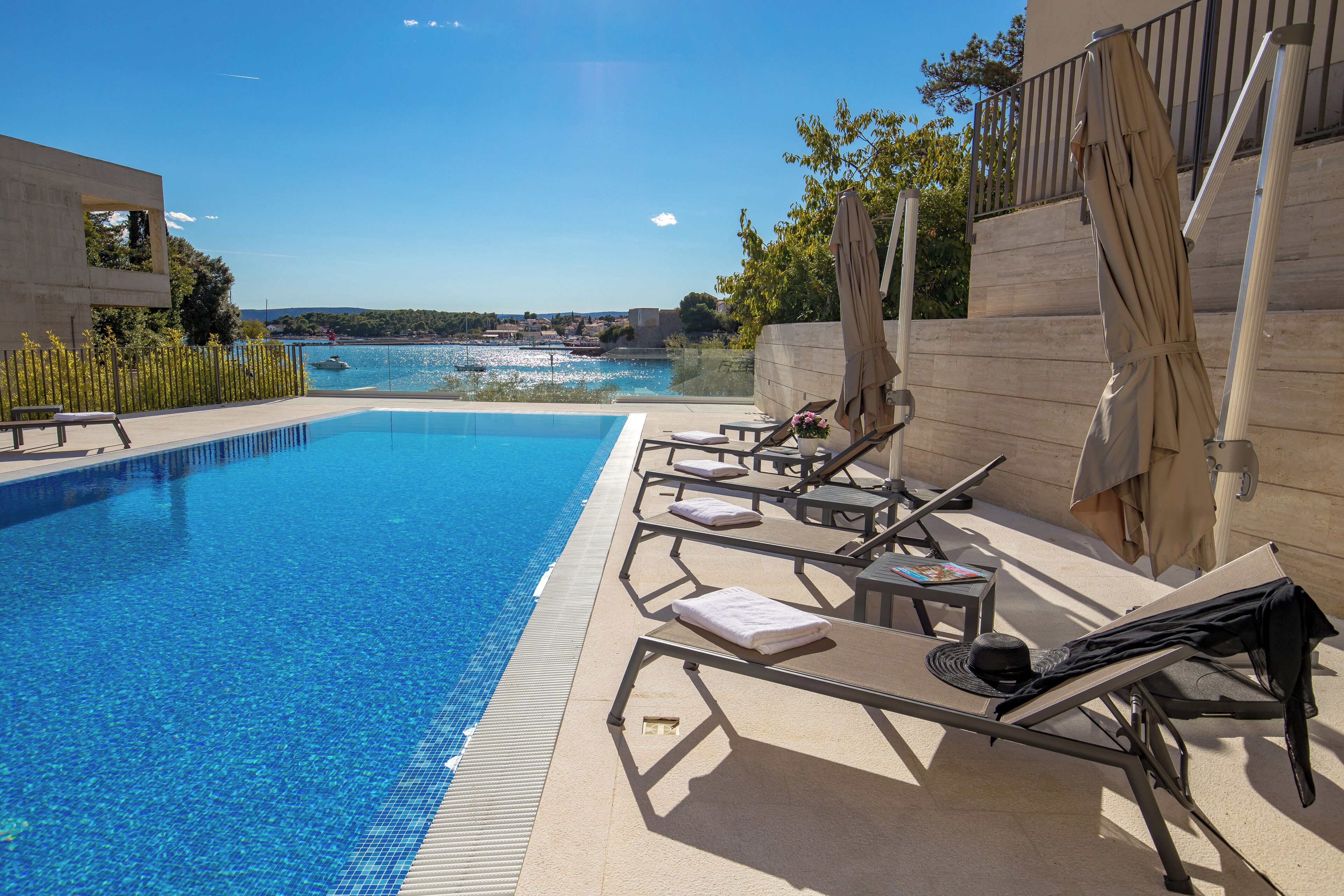 Zona de piscina con sillones, una mesita y vistas al mar.