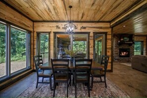 A wooden interior with a dining table, chairs, a chandelier, a fireplace, and large windows. - Broken Bow Luxury Cabin | Hot Tub | Game Room (Broken Bow)