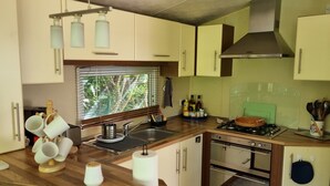 Una cucina compatta con piano cottura a gas, forno e lavello. Si notano pensili, una finestra con persiane e diversi utensili e elettrodomestici da cucina.