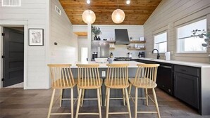 Una cocina moderna con sillas de madera, una isla central y lámparas colgantes.